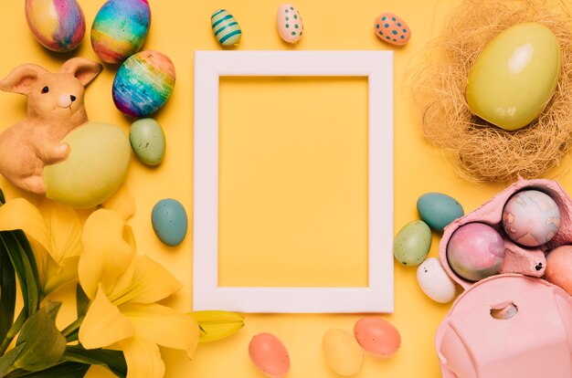 Empty white border frame decorated with easter eggs; lily flower and nest on yellow background