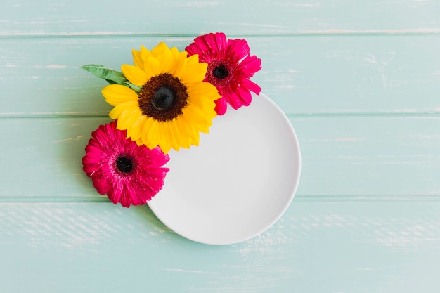 Empty white plate decorated with sunflower and gerbera flower on table