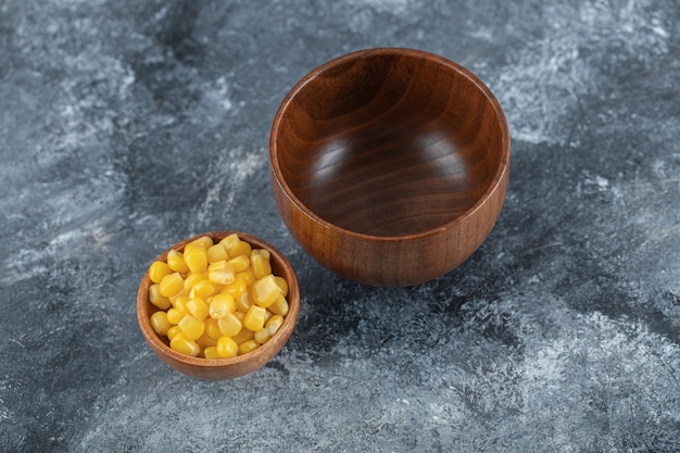 An empty wooden bowl with small bowl of popcorn seeds.