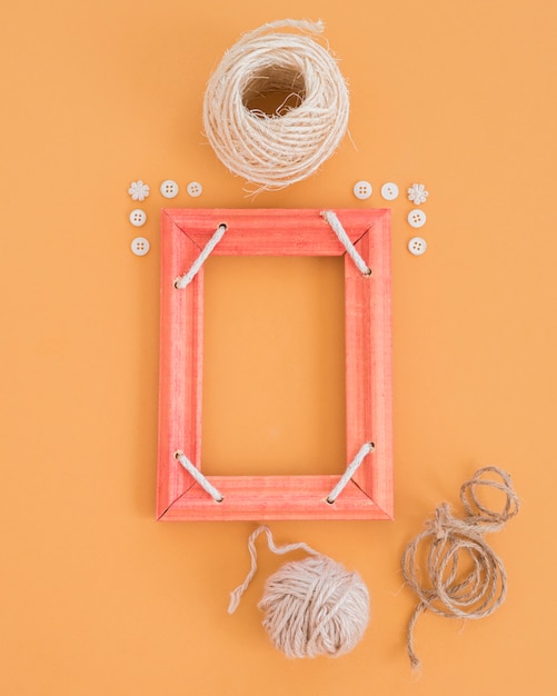 Free photo an empty wooden frame decorated with button and spools on an orange backdrop