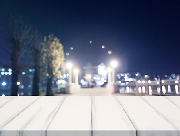 Free Photo empty wooden white table in front of blurred city lights at night