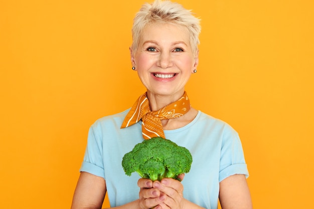 Free photo energetic beautiful middle aged woman with short gray hair posing isolated with green broccoli in her hands, going to make healthy organic salad.