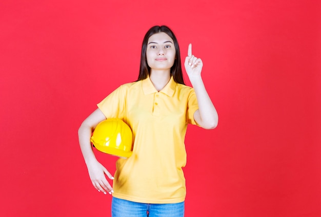 Free photo engineer girl in yellow dresscode holding a yellow safety helmet and showing somewhere