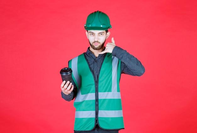 Engineer in green uniform and helmet holding a black disposable cup of coffee. 