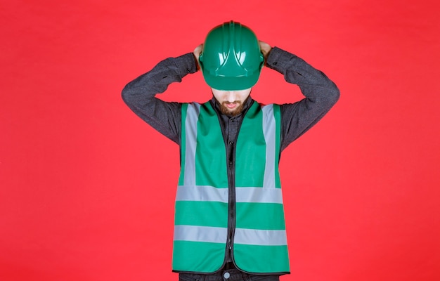 Free Photo engineer in green uniform and helmet holding his head as he is tired. 