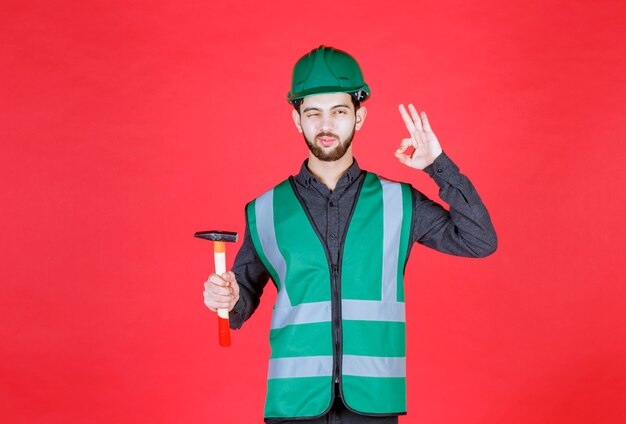 Engineer in green uniform and helmet holding a wooden ax and showing positive hand sign. 