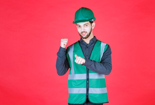 Engineer in green uniform and helmet pointing backside. 