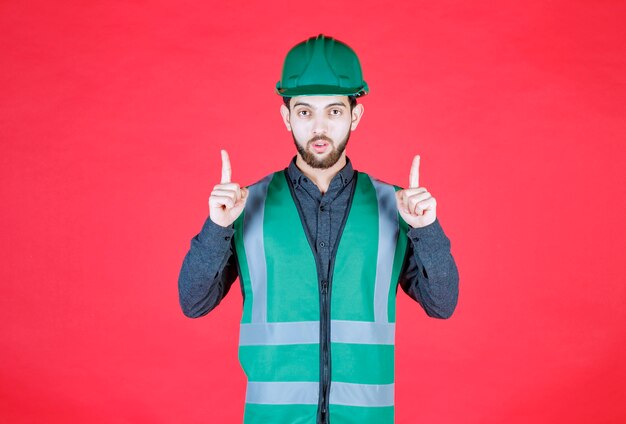 Engineer in green uniform and helmet pointing above. 