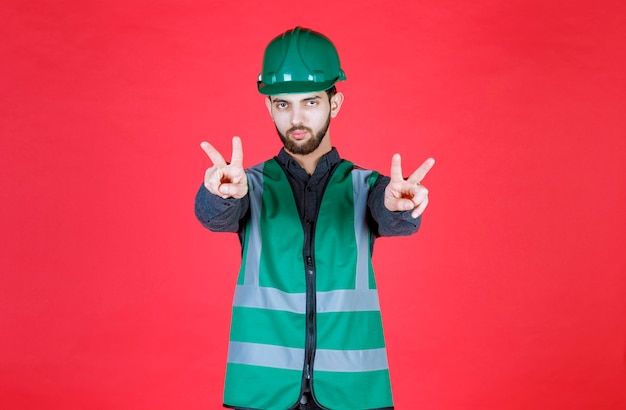 Free photo engineer in green uniform and helmet sending peace and friendship.