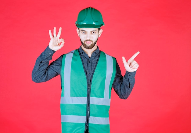 Free photo engineer in green uniform and helmet showing enjoyment sign.