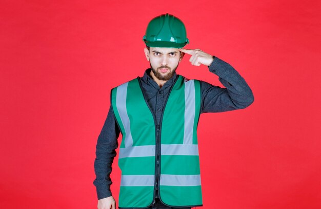 Engineer in green uniform and helmet thinking and planning. 