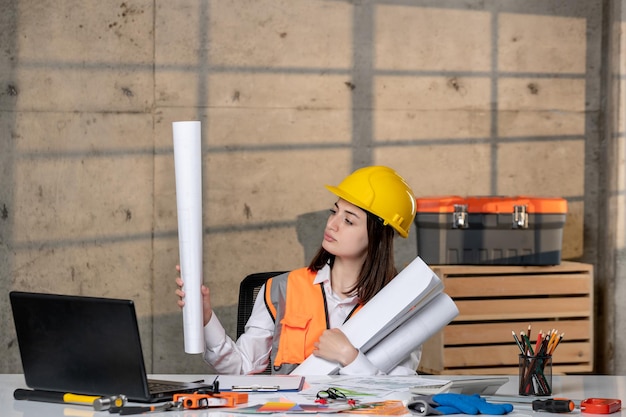 Engineer in helmet and vest civil worker smart young cute brunette girl with paper rolls