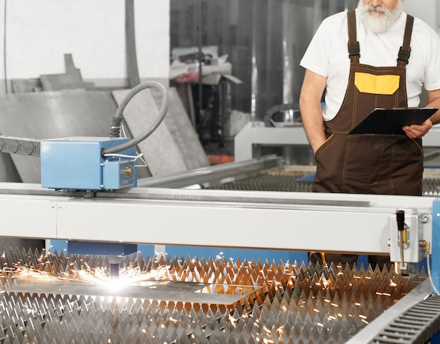 Engineer observing plasma laser cutting metal sheet.