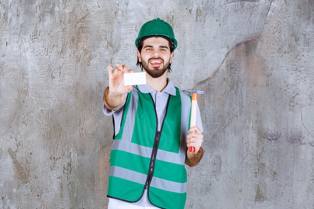 Free Photo engineer in yellow gear and helmet holding a wooden handled ax and presenting his business card. 