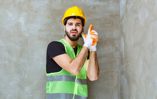 Engineer in yellow helmet and industrial gloves showing gun sign in the hand