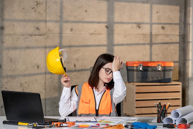 Engineer young cute smart brunette girl civil worker in helmet and vest very tired