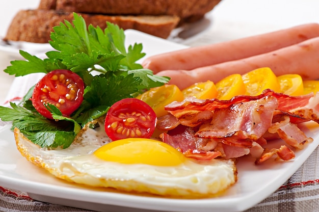 English breakfast - fried eggs, bacon, sausages and toasted rye bread