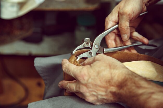 Enjoying process of craft shoes creation. Workplace of shoe designer. Hands of shoemaker dealing with cobbler tool, close up