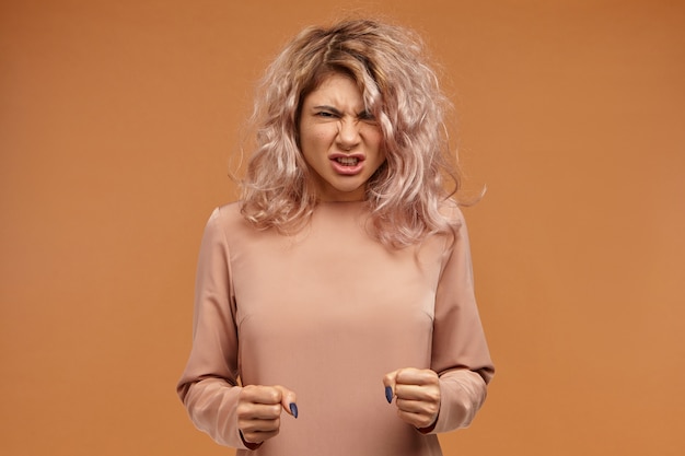 Free photo enraged furious young woman with voluminous hair clenching fists and roaring, expressing her anger