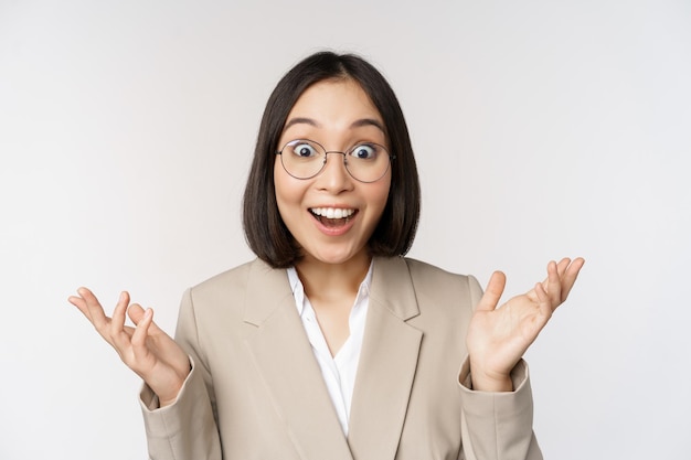 Free Photo enthusiastic asian saleswoman in glasses smiling and laughing looking amazed at camera standing in beige suit over white background