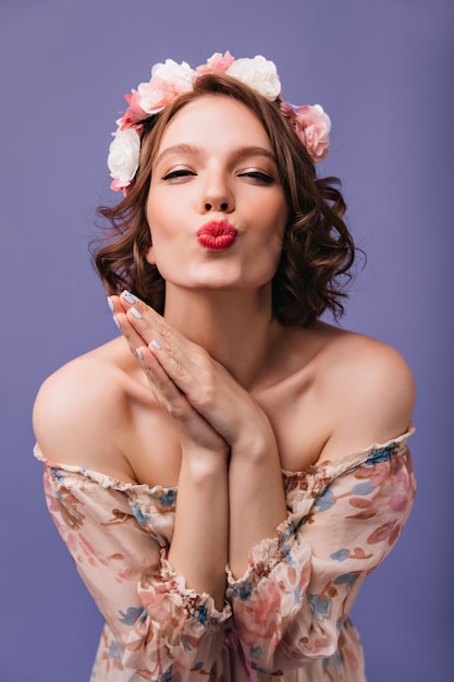 Enthusiastic beautiful girl with short hairstyle posing with kissing face expression. Indoor photo of gorgeous romantic woman with flowers in hair isolated.