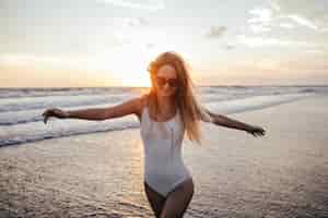 Free photo enthusiastic caucasian girl running down the ocean coast and laughing. outdoor portrait of glad woman in white swimsuit enjoying summer vacation at exotic resort.