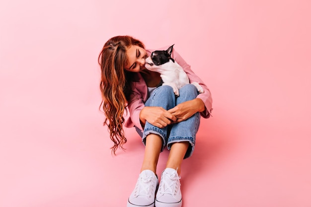 Enthusiastic girl kissing her puppy in nose Studio portrait of joyful lady looking at french bulldog with love