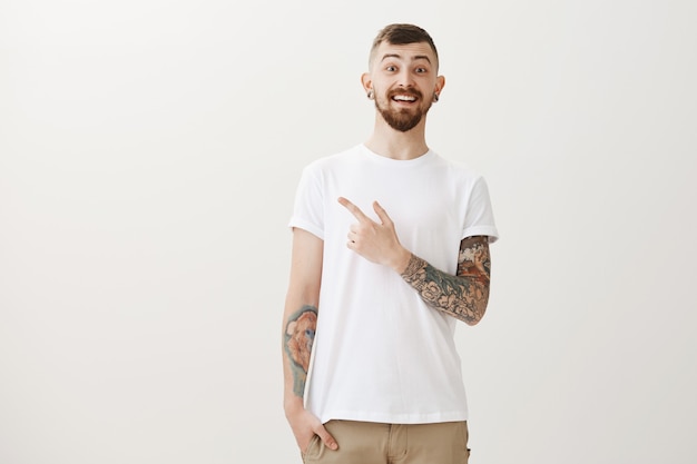 Enthusiastic handsome tattooed guy pointing finger upper left corner and smiling amazed