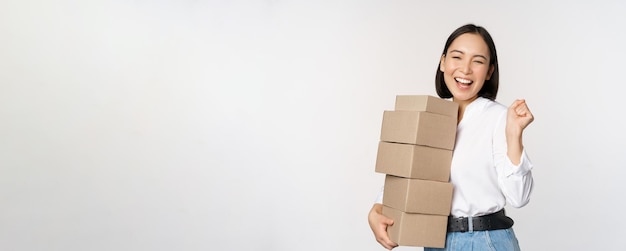 Enthusiastic korean girl shopper holding boxes delivery and smiling happy standing over white background