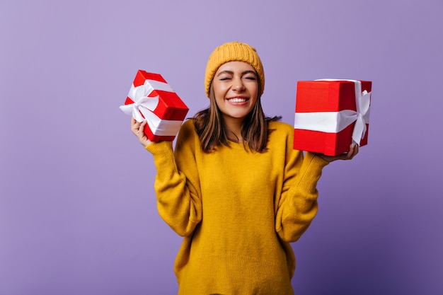 Free photo enthusiastic lady in knitted hat posing with christmas presents. cheerful birthday girl enjoying gifts.