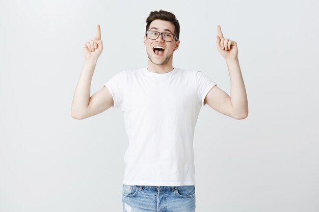 Enthusiastic male student in glasses inviting to event, pointing fingers up