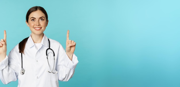 Free photo enthusiastic medical worker young woman doctor in white coat stethoscope showing advertisement point