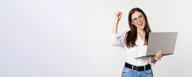 Free photo enthusiastic office woman businesswoman holding laptop and shouting with joy celebrating and rejoici