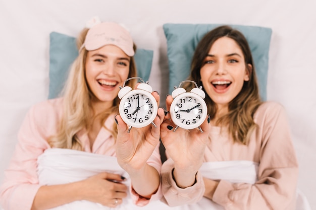 Free photo enthusiastic women in bed showing clocks