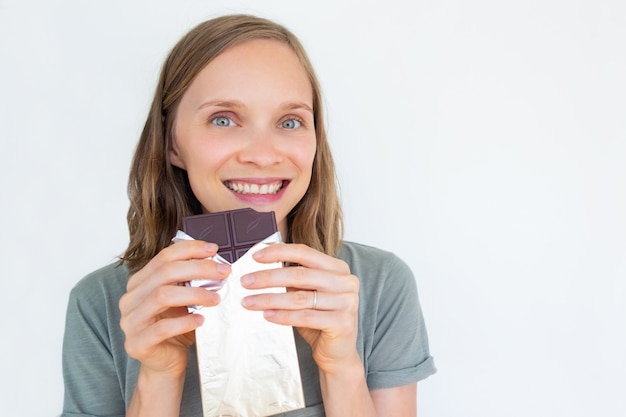 Enthusiastic young woman holding chocolate bar in gold foil