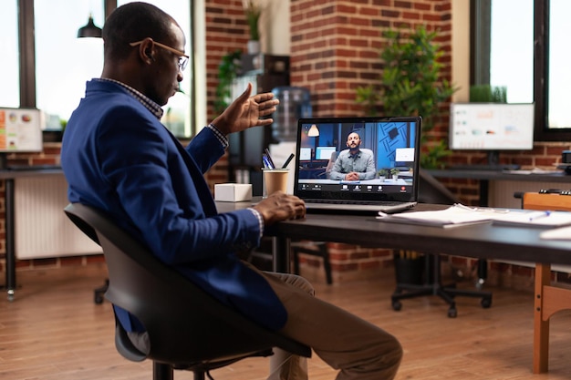 Free photo entrepreneur using video call conference on laptop to talk to colleague in startup office. business man attending online teleconference meeting with person to discuss project and strategy.