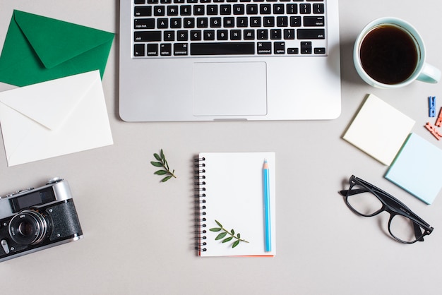 Envelope; retro camera; spiral notepad; eyeglasses and open laptop on white backdrop