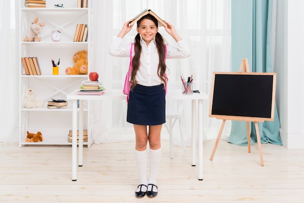 Ethnic schoolgirl standing under book roof