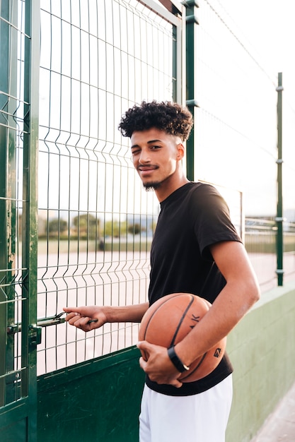 Ethnic young man winking while standing with basketball 