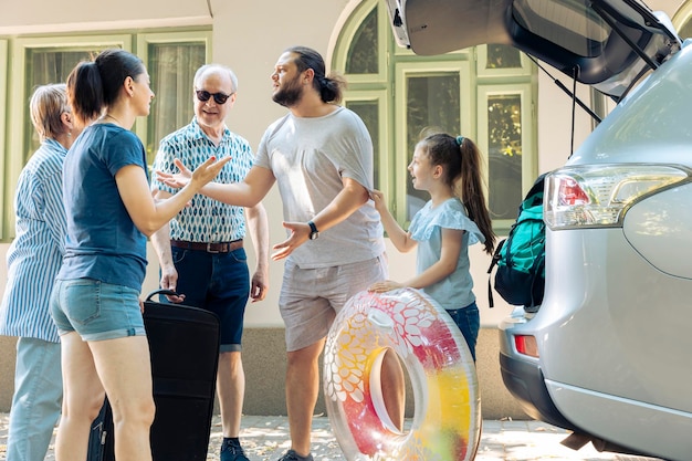 Free photo european family travelling to seaside with vehicle, going on road trip adventure with grandparents. people leaving on summer holiday, loading baggage and suitcase trolley in automobile trunk.