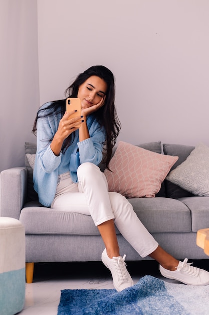 European fit brunette fashion blogger woman sits on floor in living room near sofa