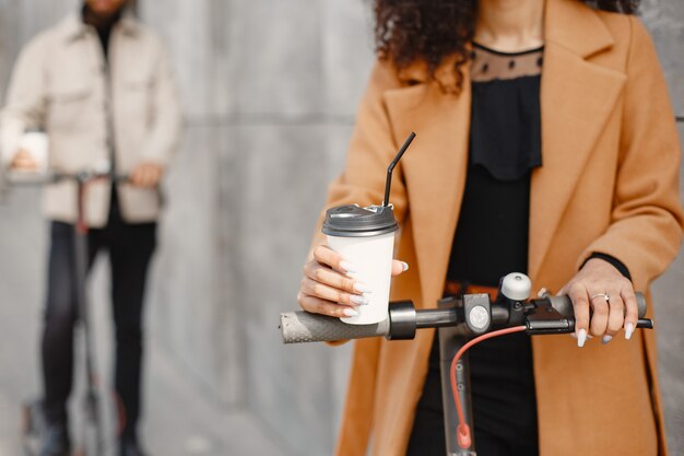 European girl anindian guy ride scooters and smile.  People with coffee.