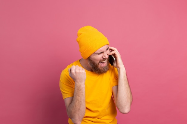 Free photo european handsome man talking on smartphone screaming proud and celebrating victory and success very excited on pink