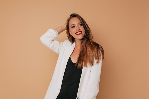 European happy woman in with bright make-up looking at camera while posing over beige background