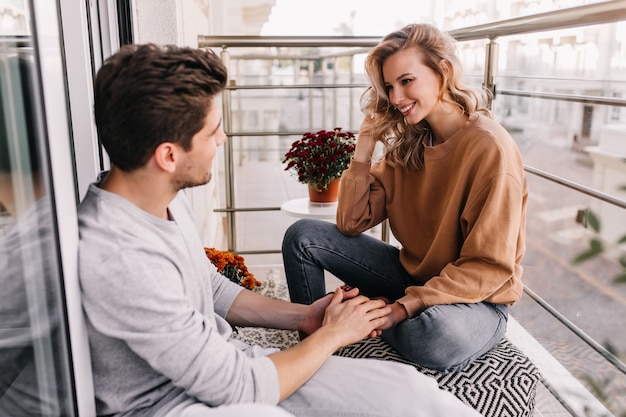 Free photo european man touching girlfriend's hands. smiling debonair woman talking with friend at balcony.