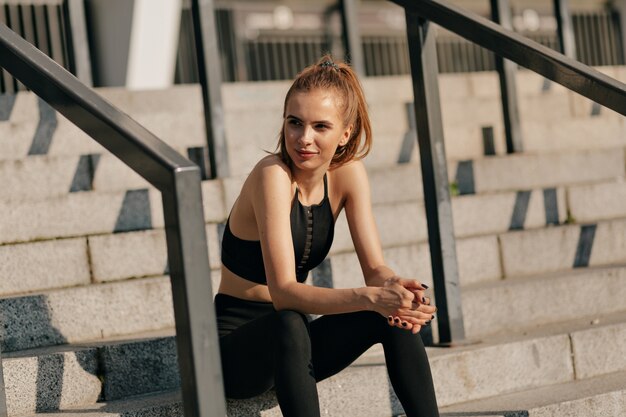 european woman in sport uniform sitting on stairs and preparing for outside training