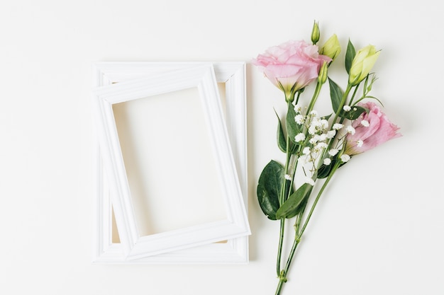 Eustoma and baby's-breath flowers near the wooden frame on white background