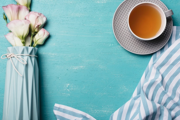 Free photo eustoma flower vase with cup of tea and napkin on blue background