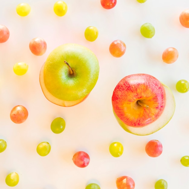 Exchange slices of green and red apple surrounded with grapes on white backdrop