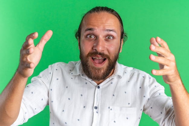 Free photo excited adult handsome man keeping hands in air looking at camera isolated on green wall